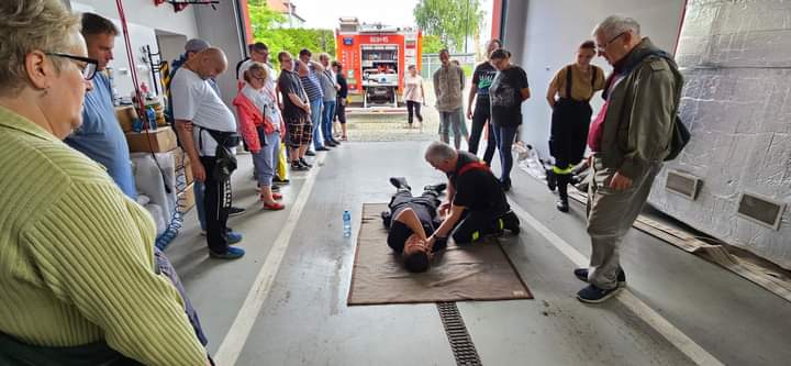 Na zdjęciu widać strażaka prezentującego ukladanie człowieka w pozycji bezpiecznej dookoła uczestnicy obserwujący pokaz.