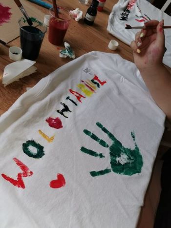 Biała koszulka z kolorowym napisem 'Wolontariusz" odbitą ręką i namalowanym sercem.