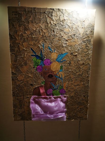 Na zdjęciu widać obraz wyklejany gazetą w centrum kobieta namalowana farbami z owocami i liścmi na głowie