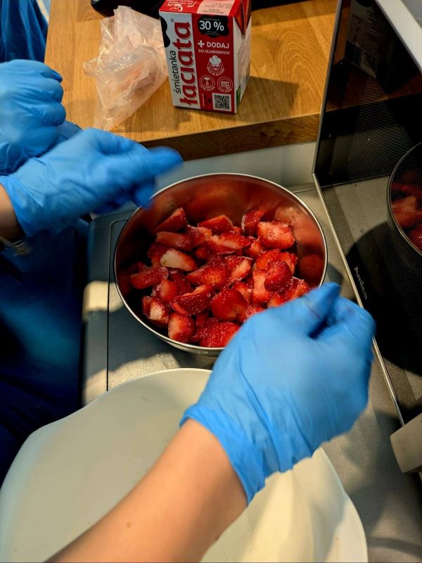 Na zdjęciu widać ręce w rękawiczkach trzymające miskę z pokrojonymi truskawkami