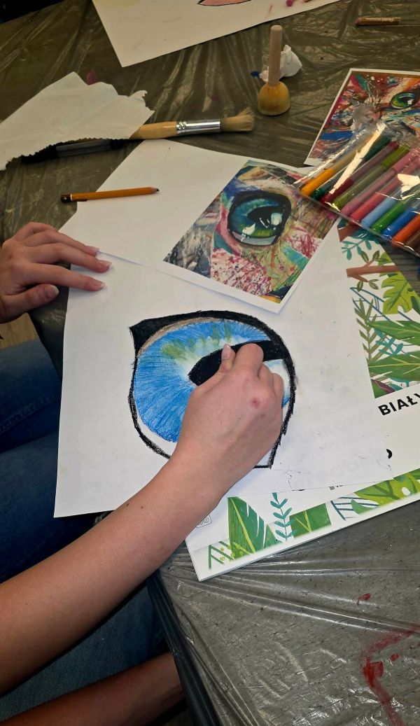 Na zdjęciu widać rękę rysująca kocie oko na białej kartce.