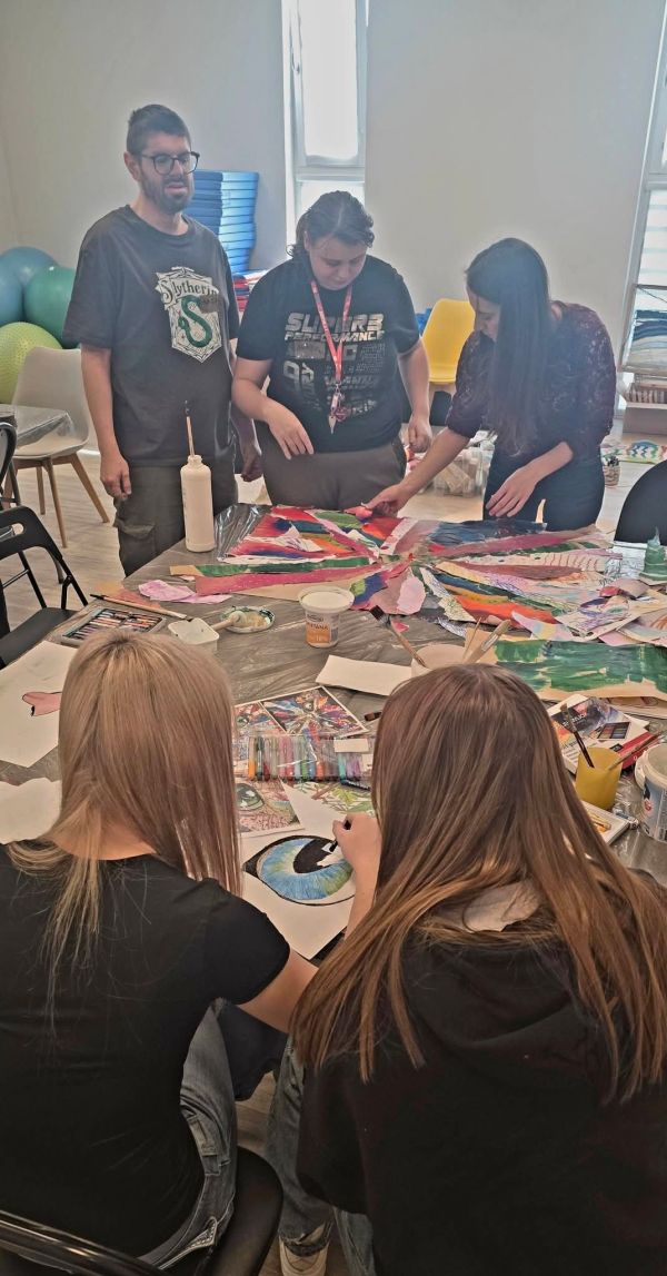 Na zdjęciu widać osoby zgromadzone wokół stołu przyklejające kolorowe kawałki do kartonu.