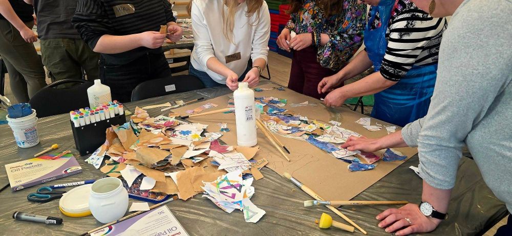 Na zdjęciu widać osoby zgromadzone wokół stołu wyklejające na kartonie obrazek.